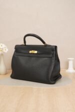 Side view of a black Hermès Kelly 35 bag with gold hardware on a surface