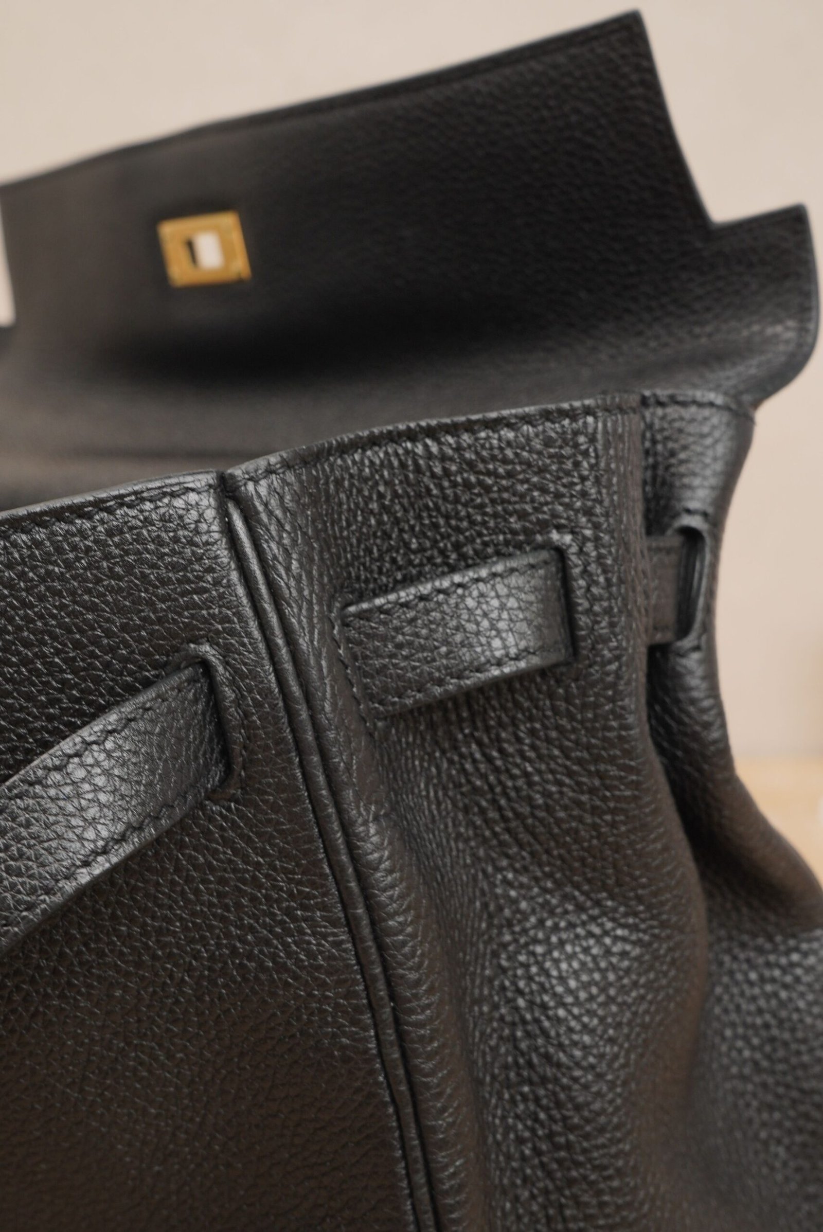 Close-up side view of a black Hermès Kelly 35 bag with gold hardware on a textured leather surface.