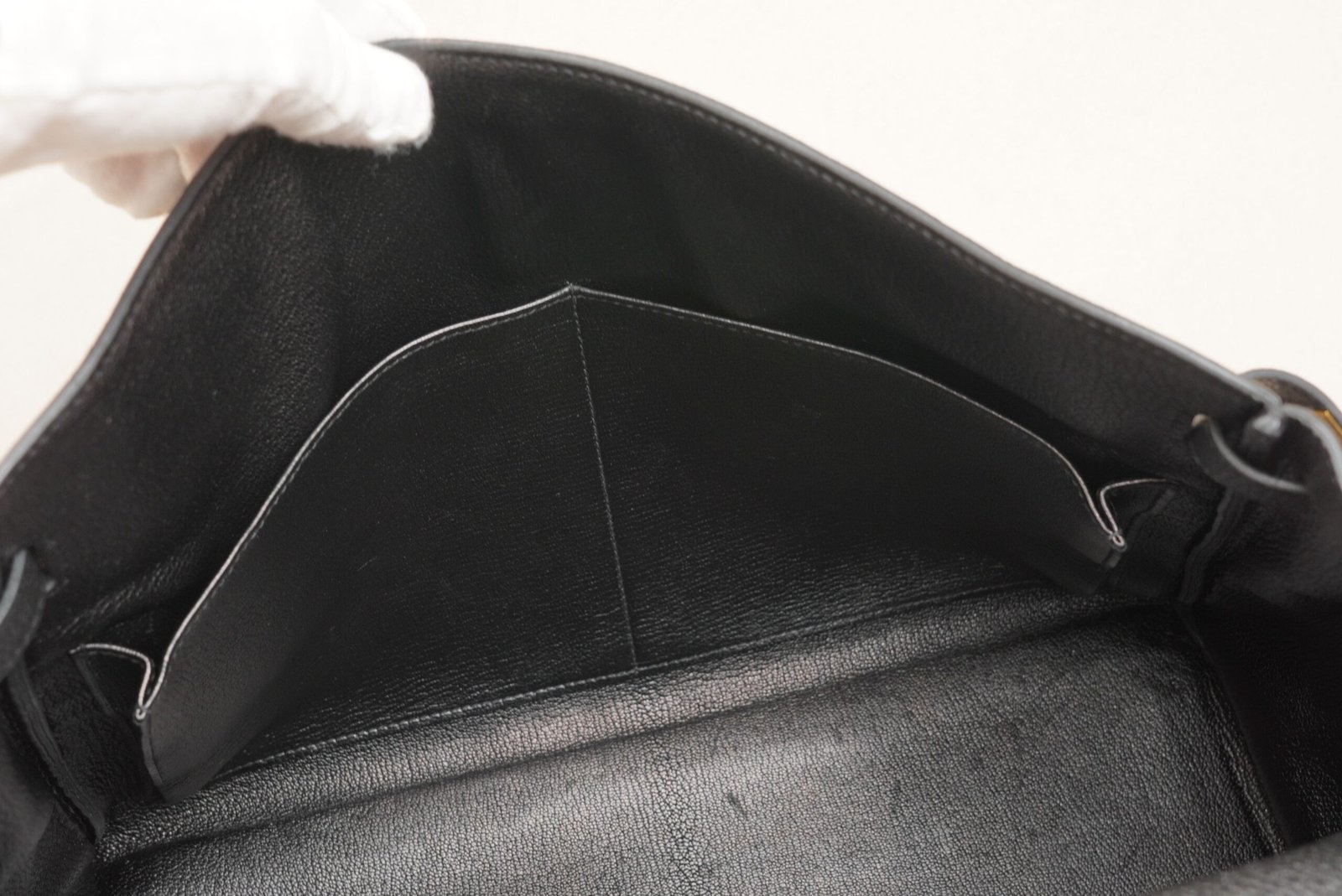 Close-up side view of a black Hermès Kelly 35 handbag with gold hardware on a surface